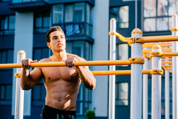 Fototapeta na wymiar Portrait of athlete young mixed race man resting after exercises on horizontal crossbar at sportsground. Handsome muscular shirtless male training hard, sportsman working out outside.