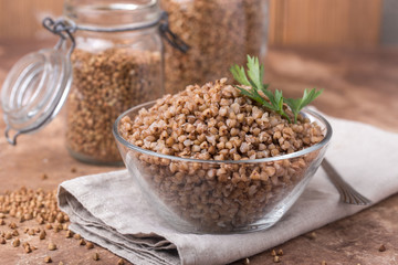 Cooked buckwheat in a glass, transparent bowl, parsley leaf, linen napkin, jars for storing cereals.