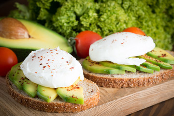 Avocado toast, cherry tomato and poached eggs on wooden background. Breakfast with vegetarian food, healthy diet concept.