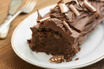 Chocolate swiss roll isolated on a wooden background. Chocolate sweet dessert. Pastry for breakfast or tea.
