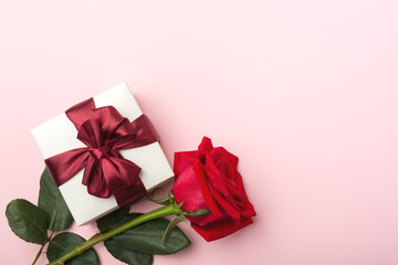 Gift in white, square box, burgundy satin ribbon, one red rose with leaves, pink paper background
