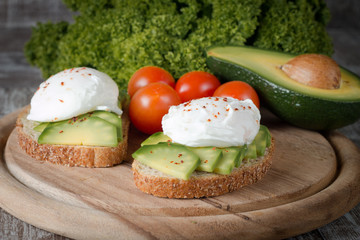 Avocado toast, cherry tomato and poached eggs on wooden background. Breakfast with vegetarian food, healthy diet concept.