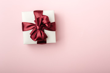 White gift box, with burgundy satin ribbon, pink background, top view, left side