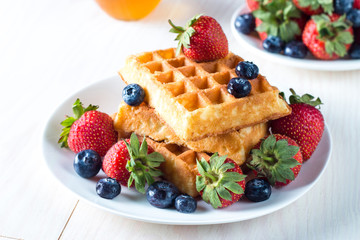 Fresh homemade food of berry Belgian waffles with honey, chocolate, strawberry, blueberry, maple syrup and cream. Healthy dessert breakfast concept with juice