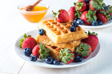 Fresh homemade food of berry Belgian waffles with honey, chocolate, strawberry, blueberry, maple syrup and cream. Healthy dessert breakfast concept with juice