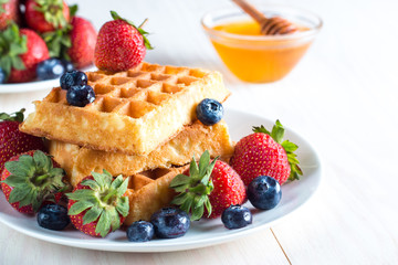 Fresh homemade food of berry Belgian waffles with honey, chocolate, strawberry, blueberry, maple syrup and cream. Healthy dessert breakfast concept with juice