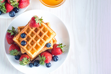 Fresh homemade food of berry Belgian waffles with honey, chocolate, strawberry, blueberry, maple syrup and cream. Healthy dessert breakfast concept with juice