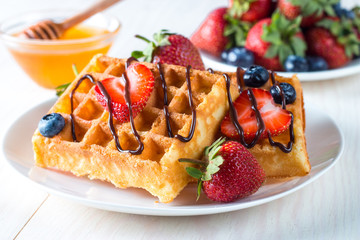 Fresh homemade food of berry Belgian waffles with honey, chocolate, strawberry, blueberry, maple syrup and cream. Healthy dessert breakfast concept with juice