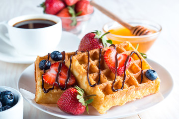 Fresh homemade food of berry Belgian waffles with honey, chocolate, strawberry, blueberry, maple syrup and cream. Healthy dessert breakfast concept with juice