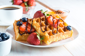 Fresh homemade food of berry Belgian waffles with honey, chocolate, strawberry, blueberry, maple syrup and cream. Healthy dessert breakfast concept with juice