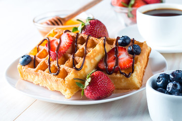 Fresh homemade food of berry Belgian waffles with honey, chocolate, strawberry, blueberry, maple syrup and cream. Healthy dessert breakfast concept with juice