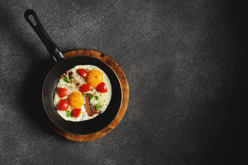 Pan of fried eggs, bacon and cherry tomatoes on dark table surface, top view 