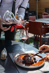 Waiter in restaurant pours a customer red wine from the decanter