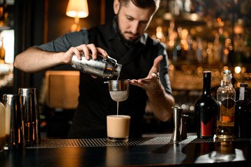 Bartender pouring cocktail with sour mix through strainer