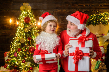 Fototapeta na wymiar Santa Claus and child with Christmas present. Kid boy and father in Santa costume and beard. Christmas, family holidays and childhood concept. Little child with Santa Claus and Christmas gift at home.