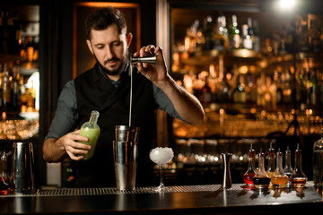 Bartender pouring cocktail with liquor using jigger and shaker