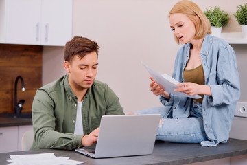 young caucasian couple hold audit of finance at home, discuss and speak sitting at home with laptop, active discussion, analyzing and calculating