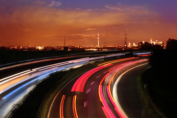Traffic with motion cars with luminous lines of speed and the evening European city of Frankfurt with beautiful sunset sky, cityscape - obrazy, fototapety, plakaty
