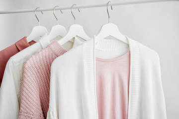 Feminine clothes in pastel pink  color on hanger on white background.  Elegant dress,  jumper,...