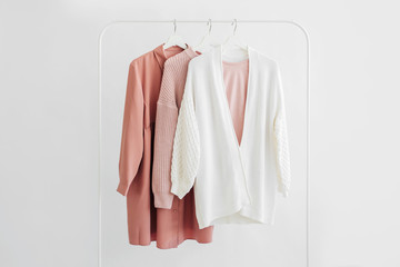 Feminine clothes in pastel pink  color on hanger on white background.  Elegant dress,  jumper, shirt and other fashion outfit. Spring cleaning home wardrobe. Minimal concept.
