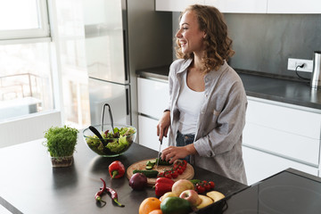 Happy young woman making a salad at the kitchen