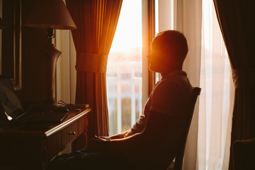 Man sitting and working on laptop on hotel room at sunset light from window - Powered by Adobe