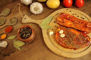 top view of raw meat, two meat pickled in spices meat medallions lie on a round wooden board on the table, garlic, bay leaf, potatoes and tomatoes nearby, cooking concept, copy space