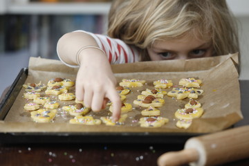 Kind nascht frech, selbstbewusst Süßigkeiten, Weihnachtsplätzchen von Backblech in Küche. - obrazy, fototapety, plakaty