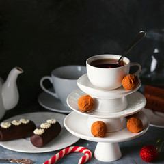 Creative concept with white dishes Christmas tree shape pyramid with cup of tea on top decorated with sweet chocolate truffles on dark background. Wallpaper or postcard about Xmas, New Year. Square