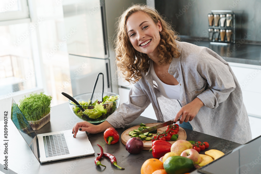 Wall mural happy young woman making a salad at the kitchen