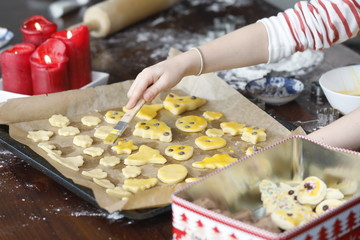 Kind backen, dekorieren, ausstechen, zubereiten, Weihnachtsplätzchen, bunte Plätzchen mit Zutaten, rote Kerze, Backblech, Holz Tisch an Weihnachten Advent