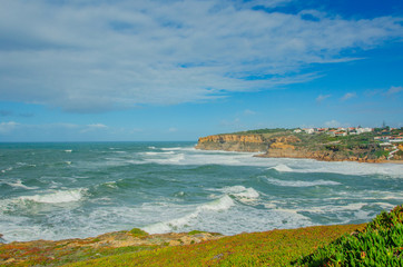 View of the Atlantic ocean, waves, picturesque village in Portugal. Panorama. Windy ocean in sunny day with bright colors.