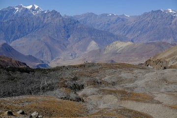 Harsh desert mountain scenery of Mustang land on trail from Thorung La Pass to Muktinath, Himalaya, Nepal. Small silhouette of tourist on ridge. During trekking around Annapurna.