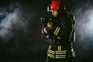 Naklejka premium young adult firefighter saving people from fire wearing uniform and helmet, holding fire fighting equipment