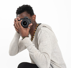 A black skin male photographer in a gray sweater and black pants is making photos with his black camera