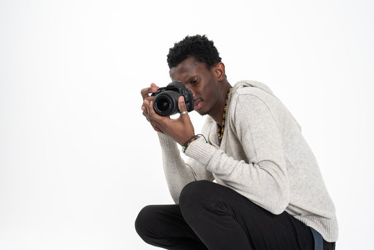 A black skin male photographer in a gray sweater and black pants is making photos with his black camera