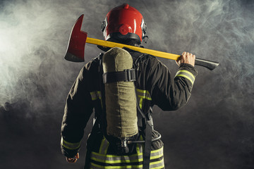 Naklejka premium rear view on extinguisher stand holding hammer isolated over smoky background, wearing red helmet and uniform