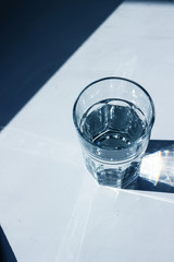 Water glass with strong shadows on white background, toned in 2020 classic blue color