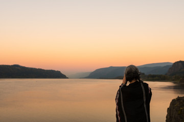Fototapeta premium A young woman with poncho takes photographs of the sunset at the Corbett lookout on the Columbia River, Oregon