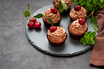 Chocolate cupcakes with ripe red cherries and cheese cream on slate plate on dark wooden background. Selective focus. Healthy food