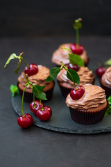 Chocolate cupcakes with ripe red cherries and cheese cream on dark wooden background. Selective focus. Unhealthy food