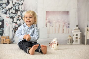 Blond toddler child, boy, reading a book at home, lying on the floor