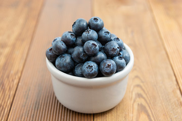 Ripe blueberries in the bowl on the wooden table. Fresh berries for breakfast.