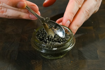 Stirring black caviar with a spoon in glass jar.