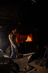 close-up of hammer and other equipment in workshop, while young man stand near furnace in the background