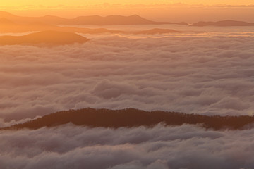 Fototapeta na wymiar Mountain tops peaking through the clouds at dawn look like islands in the sky.