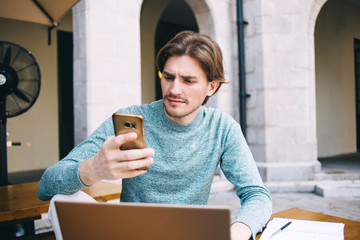 Focused male messaging on mobile and surfing laptop