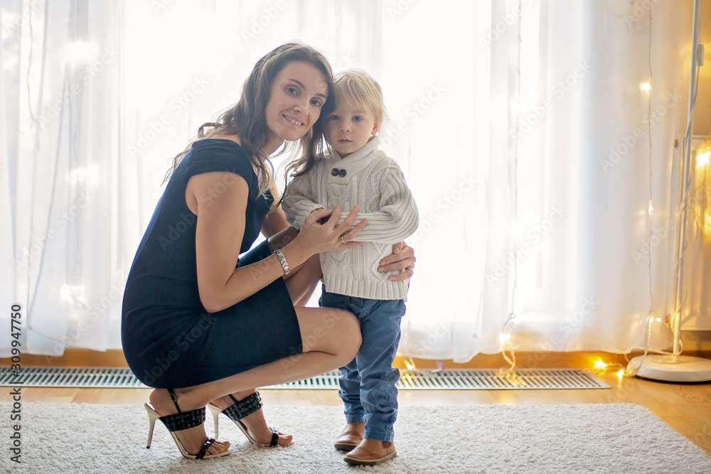 Wall mural Young mother, fashionly dressed, hugging and kissing her toddler boy