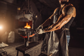 forger shop owner at work, stand heating red metal wearing gloves and apron isolated in dark space