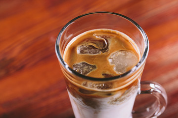 The glass cup of latte with ice on wooden table 
